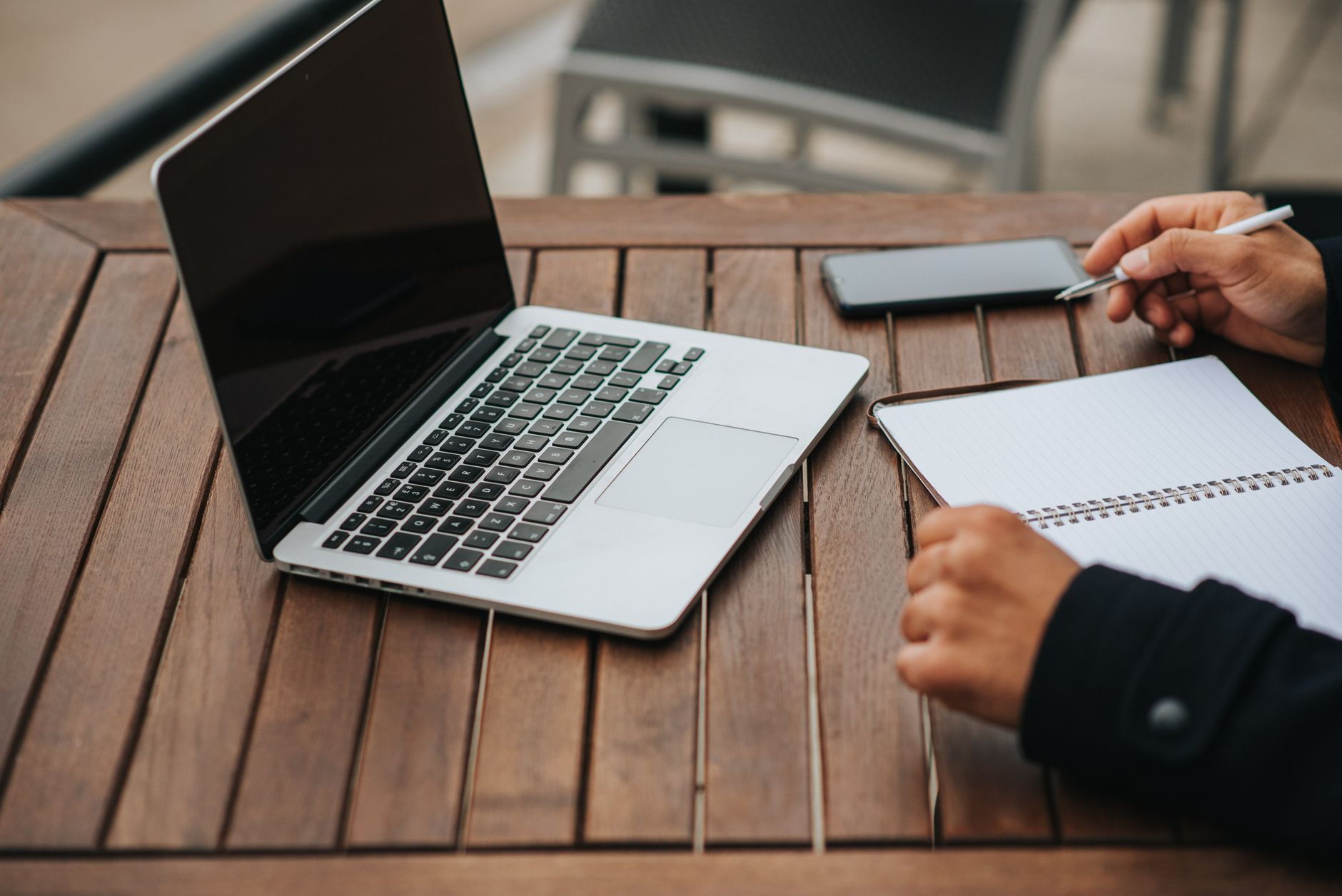 High angle of crop anonymous ethnic male entrepreneur with copybook working at cafeteria table with netbook and smartphone